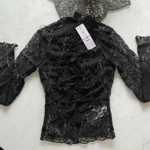 Svart spetsblus med långa ärmar XS - Säljer en svart, transparent spetsblus från Gina Tricot i storlek XS. Blusen har långa ärmar och är figurnära med vacker blommig spets och lätt rynkade detaljer. Perfekt för dig som vill ha en edgy och trendig look.