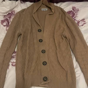 Beige kofta från Oness Mores - Säljer en beige kofta från Oness Mores i storlek XL. Koftan har snyggt stickat mönster, bred krage och fem stora knappar framtill. Materialet är mjukt och stickat, perfekt för kyliga dagar. Långärmad och med ribbade. Hör av dig vid intresse!!