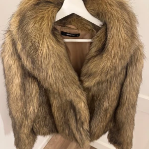 Beige pälsjacka från Gina Tricot XS - Säljer en fluffig och trendig beige pälsjacka från Gina Tricot i storlek XS. Jackan har bred krage, är helfodrad och har en snygg, naturlig look med mörkare inslag i pälsen. Perfekt för dig som vill sticka ut och hålla dig varm under kyliga dagar.