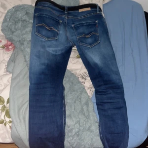 Replay Hyperflex blå jeans - Säljer ett par Replay Hyperflex jeans i klassisk blå tvätt med snygga slitningar och kontrastsömmar. Jeansen har fem fickor, raka ben och medföljande svart bälte. Stretchigt material för extra komfort och rörelsefrihet.