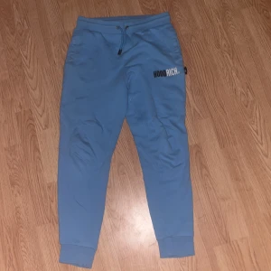 Blå mjukisbyxor från Hoodrich - Snygga blå mjukisbyxor från Hoodrich med logga på låret. Byxorna har resår och snörning i midjan samt muddar vid bensluten. Perfekta för en chill och avslappnad stil. För endast 400kr! Pris ej hugget i sten.