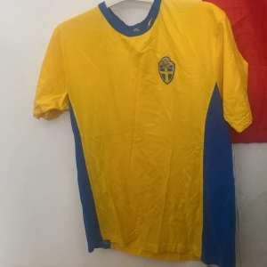 Svenska landslagets fotbollströja XL - Gul och blå fotbollströja från Svenska Fotbollförbundet i storlek XL. Klassisk design med blå detaljer vid krage och sidor samt SVFF-emblem på bröstet. Perfekt för dig som vill visa ditt stöd för Sverige på matchen eller i vardagen.