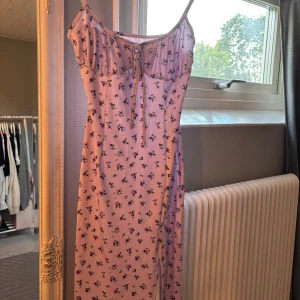 Ljuslila blommig klänning med snörning - Supersöt ljuslila klänning med små blommor och smala axelband. Den har en feminin snörning framtill vid bysten och en figurnära passform. Perfekt för varma dagar när du vill känna dig extra gullig.