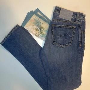 Blå jeans från Jacob Cohen - Snygga blå jeans från Jacob Cohen med klassisk femficksdesign och gul kontrastsöm. Jeansen har rak passform och knäppning med knappar framtill. Materialet är mjukt jeans-tyg i bomull. Medföljer en cool scarf med tropiskt motiv. Perfekt för dig som gillar stilrena detaljer.
