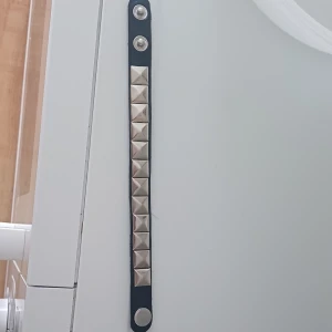 Svart nitar armband - Coolt svart armband med stora silvriga pyramidnitar och tryckknappsstängning. Perfekt accessoar för dig som gillar en edgy stil och vill sticka ut lite extra. Armbandet är smalt och sitter snyggt runt handleden. Köpte men tyckte inte att den passa mig