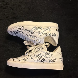 Vita sneakers Zadig & Voltaire graffiti - Unika vita sneakers från Zadig & Voltaire med coolt graffiti-inspirerat print i svart över hela skon. Skorna har snörning, platt sula och rund tå. Tillverkade i skinn för en lyxig känsla och edgy look. Perfekta för dig som vill sticka ut med din stil. Använda fåtal gånger men i väldigt bra skick! 💞 nypris runt 4000 kr, dust bag och påse ingår! 