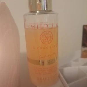 Grace Cole Wild Fig & Cranberry bath bubbles - Fräsch bath bubbles från Grace Cole med doft av vild fikon och tranbär. Flaskan är genomskinlig med guldigt lock och detaljer, och innehållet har en ljus orange ton. Perfekt för dig som gillar fruktiga och söta dofter.