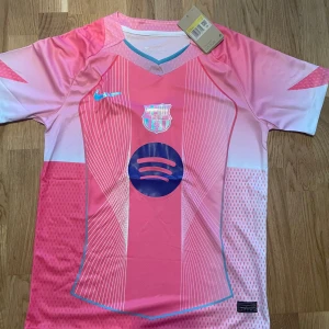 Barça x Nike rosa fotbollströja S - Säljer en limited edition FC Barcelona x Nike fotbollströja i rosa och ljusrosa med vita linjer och blå detaljer. Tröjan har korta ärmar, V-ringad krage med turkos kant och är gjord i Dri-FIT polyester. Spotify-logga och Barça-emblem på bröstet.