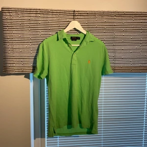Grön Polo Ralph Lauren t-shirt M - Fräsch grön t-shirt från Polo Ralph Lauren i storlek M. Klassisk pikémodell med krage, korta ärmar och två knappar vid halsen. Materialet är lätt mesh-bomull och har den ikoniska orangea Polo-loggan broderad på bröstet. Perfekt för chill dagar.