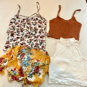 Fyra trendiga sommartoppar i olika färger - Paket med fyra snygga toppar: en vit blommig linnetopp med tunna axelband, en brun croppad topp med smock, en kort gul blommig blus med knyt framtill och en ärmlös croppad vit polotopp. Perfekta för varma dagar och att mixa olika stilar. Alla storlek s.