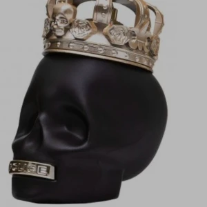 Parfymflaska i form av svart dödskalle - Unik parfymflaska från Police i form av en matt svart dödskalle med en detaljerad guldfärgad krona och metallisk detalj vid munnen. Flaskan är tillverkad i glas och metall och har en riktigt cool och edgy design.