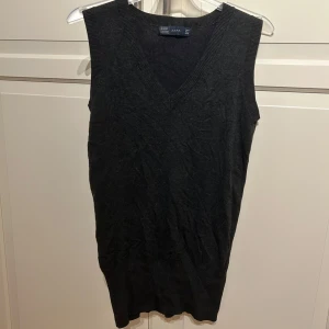 Svart stickad väst från Zara - Snygg svart stickad väst från Zara med v-ringad hals i strl M. Perfekt att bära över en skjorta eller t-shirt för en stilren look. Tillverkad i en mjuk blandning av rayon, nylon och elastan.