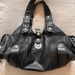 Svart handväska från Chloé - Säljer denna svarta handväska från Chloé med silverfärgade knappar och detaljer. Väskan har dubbla handtag med flätad design och fickor på sidan. Mårten är cirka i cm 40 x 20 x 15. Använd väl därav lite defekter särskilt på knapparna som blivit lite rostiga (se sista bilderna), därför också ett lägre pris! Skriv för fler bilder!