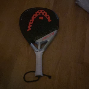 Head paddelrack - Padelracket från Head '. Snygg design med svart och rött mönster. Perfekt för dig som vill ta ditt padelspel till nästa nivå och sticka ut på banan. Greppet ser fräscht ut och racketen är i gott skick.