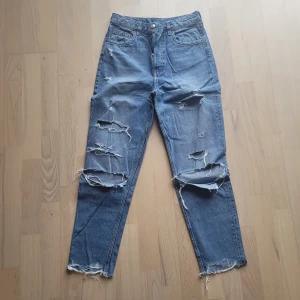 Blå slitna jeans från H&M Divided - Säljer ett par blå jeans från H&M Divided med rejält slitna detaljer och hål på benen. Jeansen har klassisk femficksdesign, raka ben och råa kanter vid benslut. Perfekta för en avslappnad och trendig look. Jeansen har haft hål som inköpta. Köpare står för frakten 