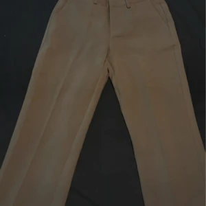 Brun Beiga kostymbyxor från Nelly - Snygga beiga kostymbyxor från Nelly med klassisk rak passform och hällor för bälte. Byxorna har diskreta bakfickor och är tillverkade i ett mjukt material som känns bekvämt hela dagen.