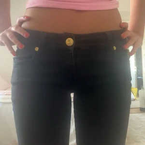 Svarta jeansbyxor med gulddetaljer - säljer dom här jättesnygga low rise flared jeansen! Jeansen luktar lite cigarr, men annars inga defekter💕