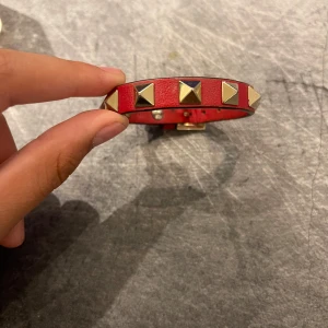 Rött valentino armband pris kan diskuteras. - Snyggt rött armband i skinn med stora fyrkantiga guldfärgade nitar runt om. Justerbart spänne för perfekt passform. Perfekt accessoar för att ge din outfit en edgy touch.