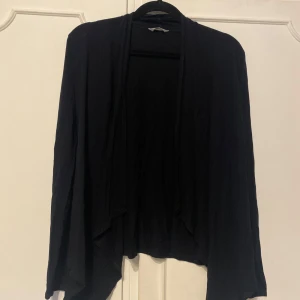 Svart kofta med öppen front - Säljer en svart, tunn och mjuk kofta med öppen front och långa ärmar. Koftan har en avslappnad passform och faller snyggt framtill. Perfekt att slänga över en topp eller klänning för en enkel och stilren look.