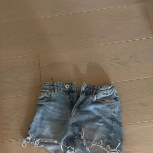 Ljusblå jeansshorts med fransar - Säljer ett par ljusblå jeansshorts med fransiga benslut och klassisk femficksdesign. Shortsen har knapp och dragkedja framtill samt låg midja. Perfekta för varma dagar!