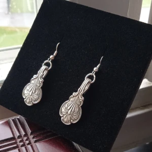 Örhängen av nysilver  - Säljer ett par snygga silverfärgade örhängen med detaljerat mönster. Hängande modell med krok. Gjord av gamla skedar. Passar dig som gillar klassiska och eleganta accessoarer som är second hand. Gjorda av mig.