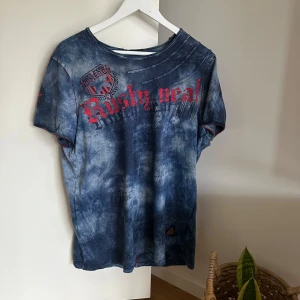 Blå y2k t-shirt  - Säljer en blå t-shirt från Rusty Neal med coolt batikmönster och rött tryck framtill. Är osäker på storleken men jag som en Xs/S person hade den som en obersize t-shirt