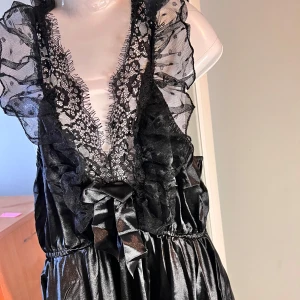 Svart sov klänning med spets och volang - Säljer en svart med djup v-ringning, spetsdetaljer och volanger upptill. Klänningen har ett brett band i midjan 