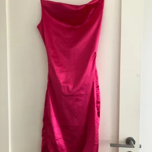 Rosa satinklänning med smala axelband - Säljer en snygg rosa satinklänning med smala axelband och rak passform. Klänningen har en elegant glansig yta och är figurnära med en enkel, stilren design. Perfekt för dig som vill sticka ut med färg.