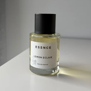 ESSNCE Lemon Eclair Parfym - Fräsch parfym i genomskinlig glasflaska med svart lock från ESSNCE. Doften heter Lemon Eclair och har en ljusgul vätska. Minimalistisk etikett med svart text och signaturdetalj. Perfekt för dig som gillar citrusdofter. Då jag är känslig för lite sötare dofter, säljer jag denna, som man ser på flaskan är den nästan helt full utan tecken på användning:)