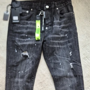 Svarta jeansbyxor med slitningar från Dsquared2 - Säljer ett par svarta jeansbyxor från Dsquared2 med coola slitningar och färgstänk. Byxorna har normal passform och klassisk femficksdesign. Perfekta för dig som vill ha en edgy och trendig look.