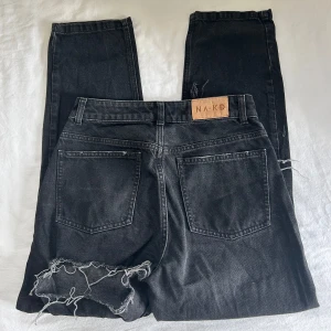 Svarta jeansbyxor från NA-KD  - Svarta jeansbyxor från NA-KD med raka ben och hål. Klassisk femficksmodell med knapp och dragkedja framtill. Byxorna är i strl 36