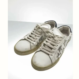 Vita sneakers med glittriga stjärnor från Saint Laurent - Säljer ett par vita sneakers från Saint Laurent med glittriga silverstjärnor på sidorna och mörkblå detalj vid hälen. Skorna har snörning och platt sula, perfekt för dig som vill sticka ut med en cool och trendig look.