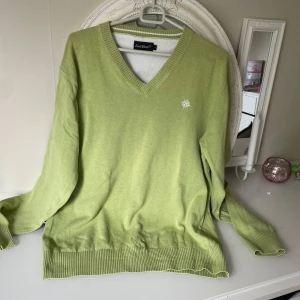 Ljusgrön v-ringad tröja från EastWest - Säljer en ljusgrön v-ringad tröja från EastWest. Tröjan har långa ärmar, ribbade muddar och en liten broderad detalj på bröstet. Perfekt för dig som gillar en klassisk och stilren look med en pop av färg.