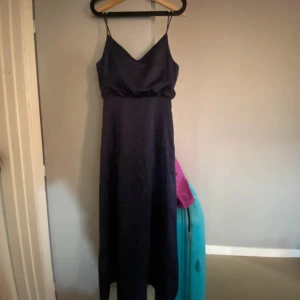 Mörkblå långklänning med smala axelband - Säljer en elegant mörkblå långklänning med smala axelband och v-ringning. Klänningen har en figurnära passform upptill och faller rakt ner. Perfekt för speciella tillfällen när du vill känna dig extra fin.