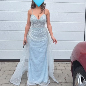Ljusblå glittrig långklänning med smala axelband - Storlek xs/S Säljer en magisk ljusblå långklänning med glittrigt tyg och smala axelband. Klänningen har öppen rygg, perfekt för bal eller fest. Materialet är syntet och klänningen har en elegant släp.