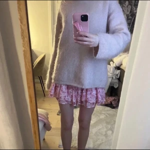 Rosa blommig volangkjol - Supersöt rosa kortkjol med blommigt mönster och volangdetaljer. Kjolen har en smockad midja som gör den bekväm och sitter snyggt. Perfekt att styla med en stickad tröja eller en enkel topp.
