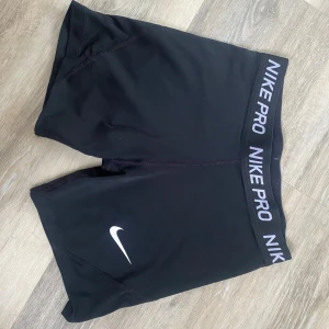 Svarta träningstights från Nike  - Säljer ett par svarta Nike träningshorts med vit logga på benet och elastisk midja med Nike tryck. Perfekta för gym eller löpning, sitter tight och bekvämt. Materialet är stretchigt och andas bra. (XL i barnstorlek) passar mig som är en S-XS 