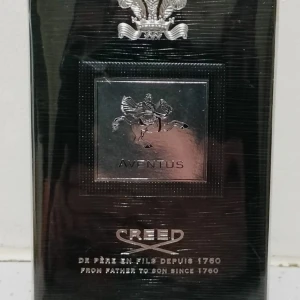 Creed Aventus Eau de Parfum - Lyxig parfym Creed Aventus i svart och silver förpackning med elegant metallplakett och klassisk logga. Doften är känd för sin fräscha, fruktiga och träiga karaktär. Flaskan och boxen har exklusiv känsla med detaljer i silver och svart. 100 ML inte ôppnad