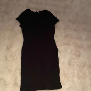 Svart ribbad lång T-shirt  från SHEIN - En svart, ribbad lång T-shirt  från SHEIN med rund halsringning och korta ärmar. T-shirten har en slim passform och är tillverkad i ett stretchigt material som sitter snyggt på kroppen. Perfekt för dig som gillar en enkel och stilren look.