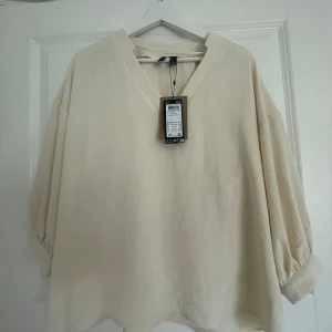 Beige blus med v-ringning från Veramoda - Säljer en luftig och stilren beige blus från Vera moda. Blusen har v-ringad hals, trekvartsärmar med lätt puff och breda muddar. Tillverkad i ett mjukt linnematerial som ger en avslappnad och trendig look.