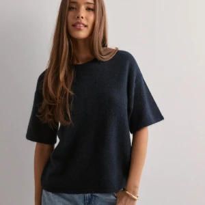 Mörkblå stickad tröja med kort ärm - Eftertraktad enkel och stilren mörkblå stickad tröja med korta ärmar och rund hals. Perfekt till jeans för en avslappnad look. Mjuk och skön känsla, passar dig som gillar minimalistisk stil.  Nypris 419kr, aldrig använd.