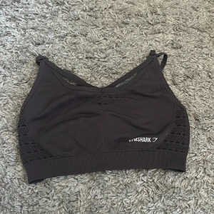 Svart sportig linnetopp från Gymshark - Svart linnetopp från Gymshark med smala, justerbara axelband och snygga meshdetaljer på sidorna och ryggen. Toppen har croppad passform och bred ribbad kant nedtill, Passar både S och Xs