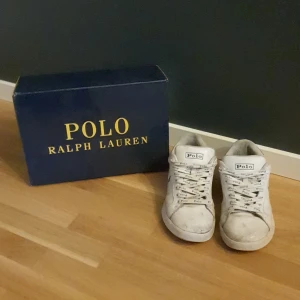 Vita sneakers från Polo Ralph Lauren - Klassiska vita sneakers från Polo Ralph Lauren med logga på plös, häl och sula. Skorna har snörning med Polo-tryck på skosnörena och en rund tå. Snygg och enkel design som passar till det mesta.