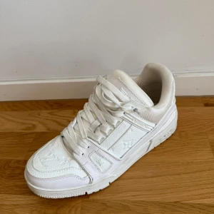 Vita Louis Vuitton sneakers  - Exklusiva helvita Louis Vuitton sneakers i skinn med präglad LV-logga och monogramdetaljer. Snygg chunky sula, rund tå och klassisk snörning. Perfekta för dig som vill sticka ut med lyxig streetstyle.