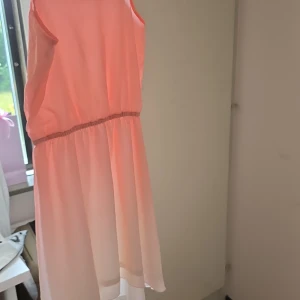 Ljusrosa sommarklänning från KappAhl - Söt ljusrosa kortklänning från KappAhl med tunna axelband och resår i midjan. Klänningen har en flowy kjol och är tillverkad i ett lätt, syntetiskt material som passar perfekt för varma dagar.