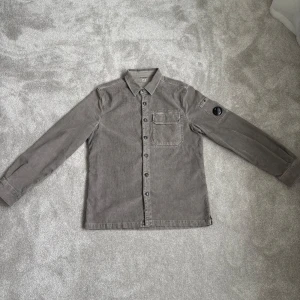C.P. Company overshirt - Hej! Säljer nu min snygga C.P. Company overshirt i manchestertyg. Overshirten är i färgen grön med lite toner av grå, riktigt snyggt! Modellen är klassisk med bröstficka och knappar hela vägen. C.P. Companys ikoniska linsdetalj finns på ärmen. Storlek är large.