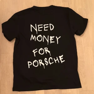 Svart t-shirt med tryck 'Need Money For Porsche' - Svart t-shirt från Gildan med stort vitt tryck på ryggen där det står 'Need Money For Porsche' i en cool, handskriven stil. Klassisk rund hals och korta ärmar. Perfekt för dig som gillar statement-plagg och streetwear vibes.