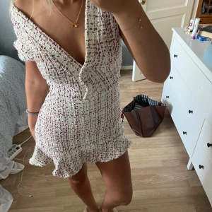 Vit och rosa kort omlottklänning - Supersöt kort klänning i vit och rosa tweed-look med omlott och v-ringning. Klänningen har volangkant nertill och är figurnära med korta ärmar. Perfekt för dig som vill ha en chic och trendig stil med lite Paris-vibe.