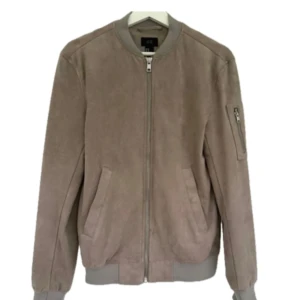 Beige mocka bomberjacka från H&M - Snygg beige bomberjacka i mocka från H&M i S. Jackan har klassisk bombermodell med ribbade muddar, dragkedja framtill och en extra ficka med dragkedja på ärmen. Mycket sparsamt använd!!