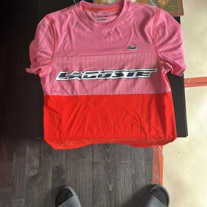 Rosa och röd Lacoste Sport t-shirt - Snygg t-shirt från Lacoste Sport x Daniil Medvedev i rosa och rött med stor Lacoste-logga på bröstet och klassisk krokodilpatch. Regular fit, kortärmad och tillverkad i bomull och mesh för extra komfort. Perfekt för dig som gillar sportig stil.